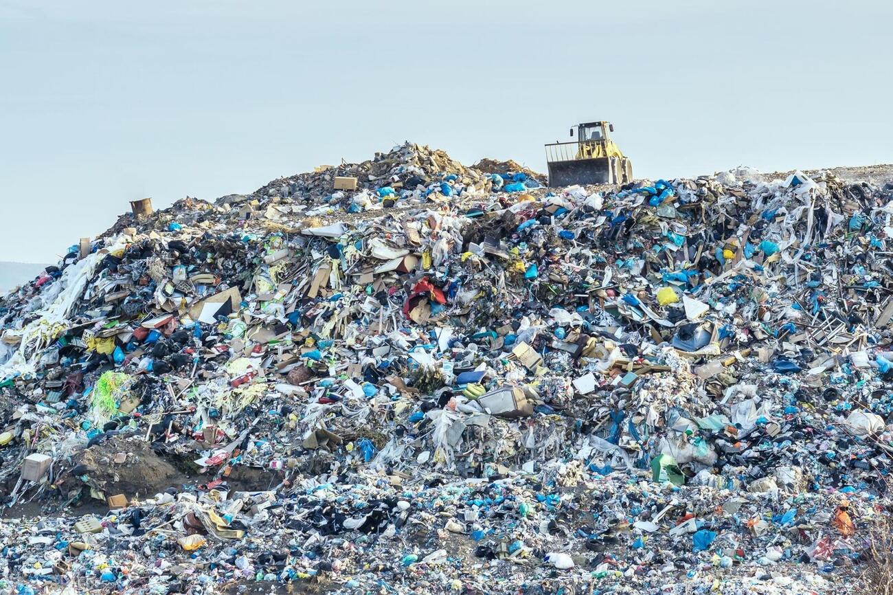 A bulldozer on top of a huge landfill heap of mixed plastic and other waste